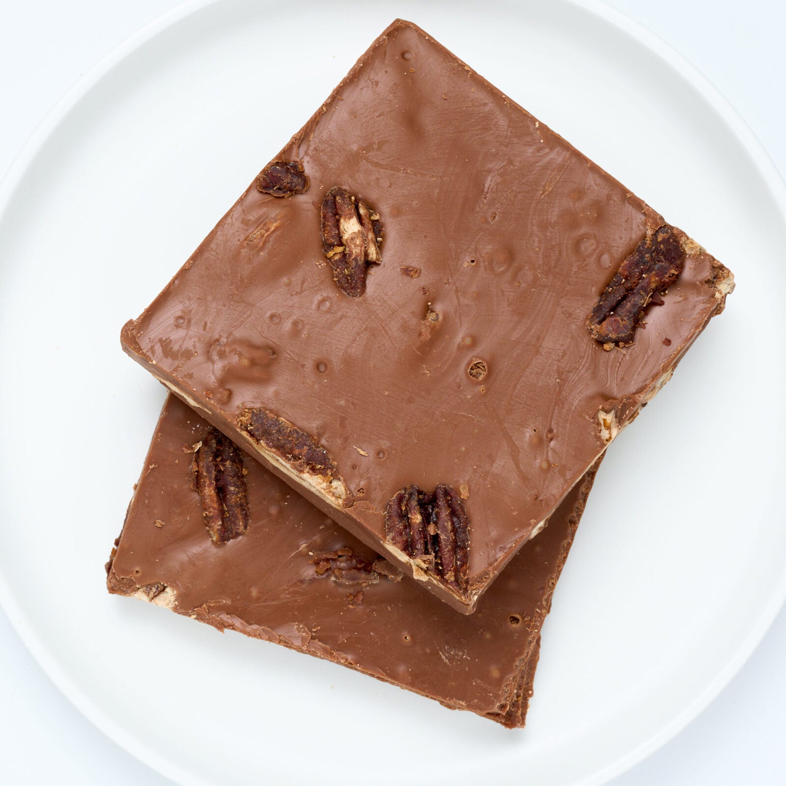 Milk chocolate pecan bark, large square pieces studded with whole pecans, on a white round plate.