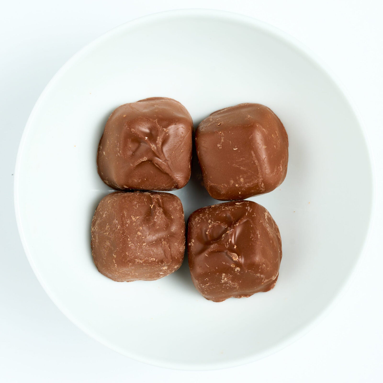 Milk chocolate covered caramel candies, square chocolate-coated pieces, arranged on a white round plate.