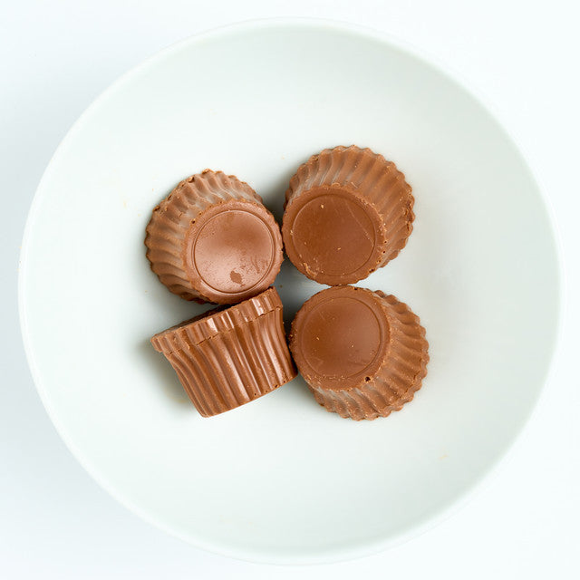 Milk chocolate covered peanut butter cups with fluted edges, arranged on a white round plate, top view.