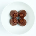 Four dark chocolate covered truffles with embossed crown tops, arranged on a white round plate.