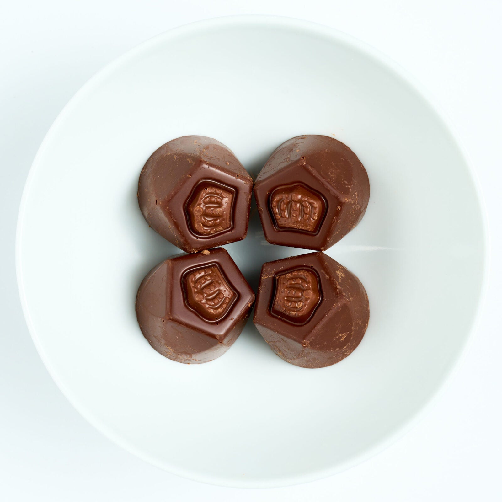 Four dark chocolate covered truffles with embossed crown tops, arranged on a white round plate.
