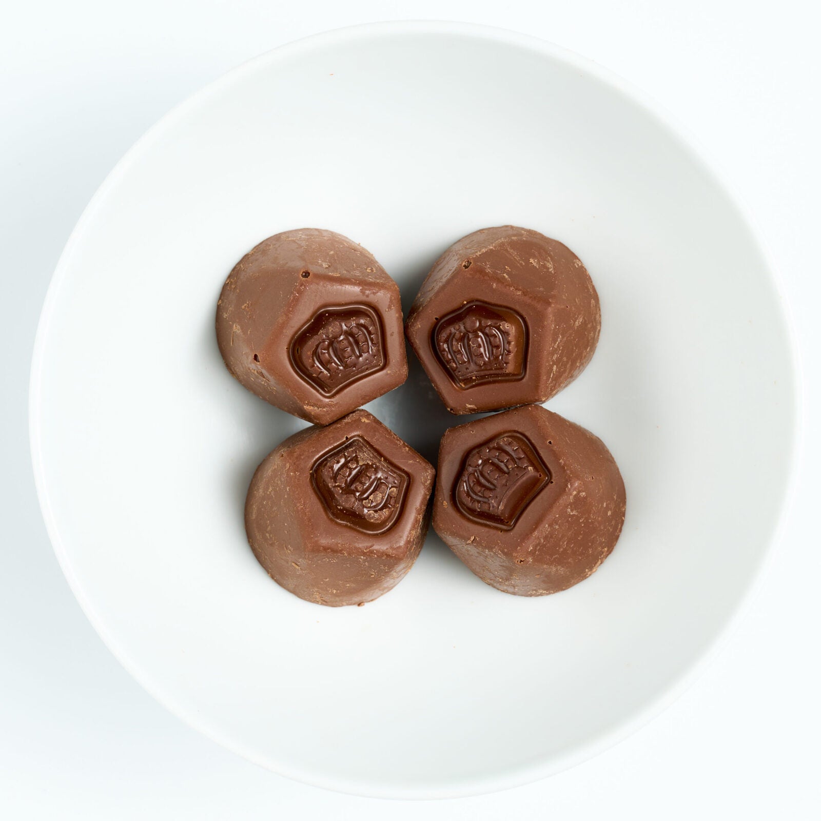 Four milk chocolate covered truffles with embossed crown tops, arranged on a white round plate.
