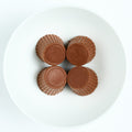 Four sugar free milk chocolate peanut butter cups with fluted edges, arranged on a white round plate, top view.