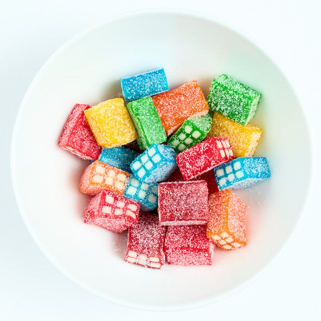 Sugar-coated fruit flavored licorice block candies in red, orange, yellow, green, and blue, piled on a white plate.