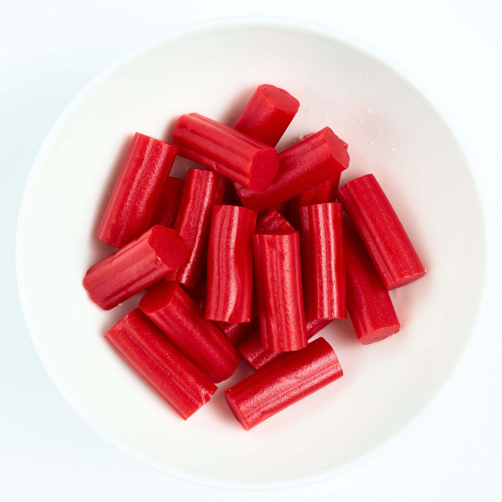 Bite-size red strawberry licorice pieces with ridged edges, piled on a white plate.