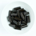 Bite-size black licorice block pieces with ridged edges, piled on a white plate.