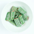 Sour watermelon block licorice pieces with green sugar-coated outside and pink center, piled on a white plate.